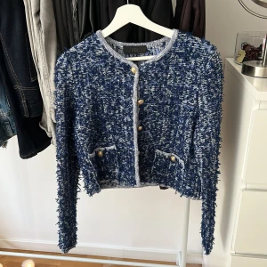 Tweedjacka från Zara  - Säljer en blå och vit kofta från Zara med cool textur och guldiga knappar framtill. Koftan har två fickor, rund halsringning och långa ärmar. Perfekt för dig som vill ha en statement piece i garderoben!