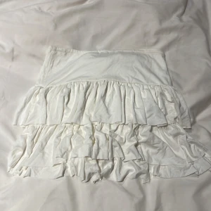 Vit volangkjol i bomull - Supersöt vit kortkjol med dubbla volanger som ger en riktigt flowy känsla. Kjolen är gjord i mjuk bomull och har en enkel, elastisk midja. Perfekt för dig som vill ha en luftig och trendig look till sommaren eller våren.