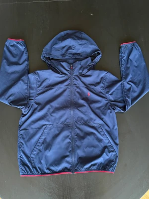 Marinblå vindjacka men även vattentålig från Polo - Vattentät vindjacka från Polo Ralph Lauren i storlek 14-16 år men är lite liten i storleken. Väldigt bra skick på jackan!