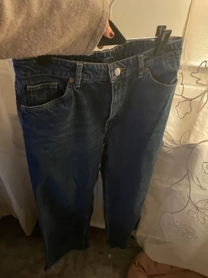Blå jeans från Monki, storlek 29 - Säljer ett par klassiska blå jeans från Monki i storlek 29. Modellen har raka ben, fem fickor och knappstängning fram. Jeansen är tillverkade i 100% bomull och har en snygg mörkblå tvätt med kontrastsömmar. Perfekt för dig som gillar enkel och tidlös stil.