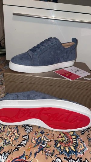 Blå mocka Christian Louboutin Sneakers - Säljer ett par stilrena blå sneakers från Christian Louboutin i mjuk mocka med klassisk röd sula och vita kanter. Skorna har rund tå, platt sula och snörning. Perfekta för dig som vill ha något exklusivt och snyggt till vardagslooken.