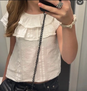 Vit blus med volang och struktur - Säljer en söt vit blus med volangdetaljer vid halsen och ett strukturerat tyg. Blusen är kortärmad och har en lätt, luftig känsla som passar perfekt till jeans eller kjol. Volangen ger en extra touch och gör toppen riktigt charmig . Den är i storlek 134/140 Men skulle söga att den sitter som xxs