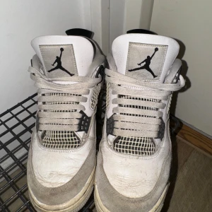 Nike Air Jordan 4 Retro Vit/Svart - Nike Air Jordan 4 Retro sneakers i vit och svart med klassisk Jumpman-logga på plösen. Skorna har meshpaneler, snörning och detaljer i syntet och skinn. Snyggt kontrasterande svart häl och platt sula. Perfekt för dig som gillar streetwear och ikoniska modeller.