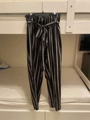 Svarta randiga byxor  - Svarta byxor från Shein med vita vertikala ränder och hög midja. Byxorna har ett midjeband. Materialet känns lätt och skönt mot huden, perfekt för en chill och snygg look.