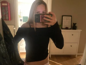 Svart offshoulder topp med rynkade sidor - Säljer en svart offshoulder topp med långa ärmar och snygga rynkade detaljer på sidorna. Toppens passform är tight och den är croppad, vilket ger en cool och trendig look. Perfekt för dig som gillar stilrena plagg med en twist.