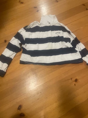 Randig pikétröja från H&M i marinblått - Säljer en snygg pikétröja från H&M med breda marinblå och vita ränder. Tröjan har lång ärm, krage och halv dragkedja framtill. Perfekt för dig som gillar sportig och avslappnad stil. Materialet är mjuk bomull som känns skönt mot huden.