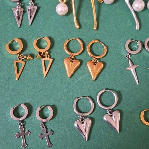 Mixade örhängen med hjärtan och kors - 75sek/par Säljer ett gäng coola örhängen i både guld och silver. Det finns olika former som hjärtan, kors, trianglar och stjärnor, samt några med pärlor och taggiga hjärtan. Perfekt för dig som gillar att mixa och matcha statement-smycken med edgy vibe.
