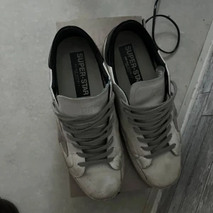 Vita sneakers med stjärndetalj - Snygga vita sneakers från Golden Goose med en grå stjärna på sidan och svarta detaljer vid hälen. Skorna har grå snörning och en rund tå. Pris kan diskuteras!!!