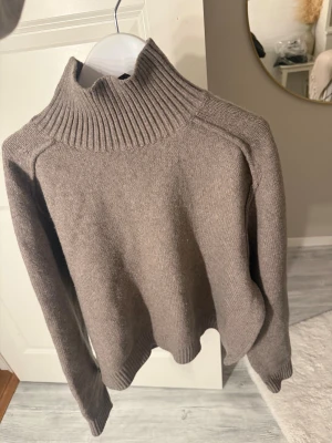 Beige stickad polotröja - Säljer en beige stickad polotröja med ribbad hög krage och långa ärmar. Tröjan har en enkel och clean look med ribbade muddar vid ärmslut och nederkant. Perfekt för dig som gillar neutrala färger och vill ha en mysig tröja till garderoben.