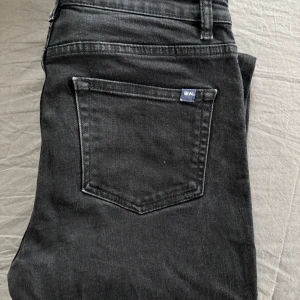 Svarta jeansbyxor från WoodWood - Säljer ett par svarta jeans från WoodWood. Jeansen har normal passform och är tillverkade i ett mjukt denimtyg. Perfekta för en stilren och enkel look.