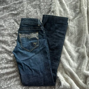 Mörkblå jeans från Guess med broderi - Snygga mörkblå jeans från Guess med coolt broderat mönster på bakfickan och klassisk logga. Jeansen är bootcut och har snygga kontrastsömmar. Perfekt för dig som gillar detaljer och vill sticka ut lite extra. Dom sitter väldigt smickrande och får mycket komplimanger i dom men tyvärr har dom nu blivit för små😣 Pris kan diskuteras vid snabb affär
