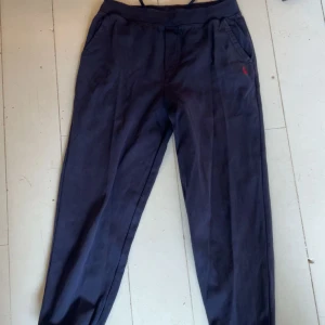 Mörkblå mjukis från Ralph Lauren - Snygga mörkblå mjukis från Ralph Lauren med klassisk passform och diskret röd logga broderad vid fickan. Byxorna har snedställda fickor fram och är tillverkade i ett mjukt bomullsmaterial. Perfekta för en stilren och avslappnad look. L i barn storlek 15-16 år 