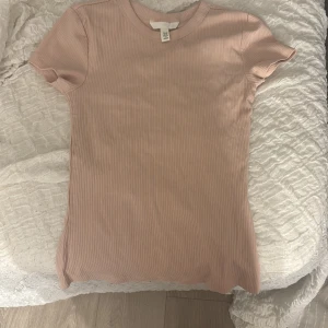 Ljusrosa ribbad topp från H&M - Supersnygg ljusrosa ribbad topp från H&M med rund hals och korta ärmar. Modellen är slim och sitter tajt mot kroppen, perfekt för dig som gillar en enkel men fräsch look. Materialet är mjukt och stretchigt, vilket gör den skön att bära hela dagen. säljer den pågrund av att ja aldrig använt den och den är i helt nytt skick.💗
