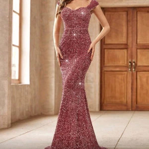 Glittrig rosa långklänning med paljetter - Bal långklänning i rosa med massor av glittrande paljetter. Klänningen har figurnära passform, markerad midja och lätt utsvängd nederdel. Snygg sweetheart-ringning och breda axelband ger en elegant look. Jag har använt klänningen en gång - på min studentbal. 