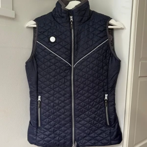 Mörkblå ridväst från Uhip - Quiltad mörkblå rid-dunväst från Uhip. Västen har två fickor med dragkedja, reflekterande detaljer och snyggt mönster i form av små rutor. Nästan aldrig använd💖