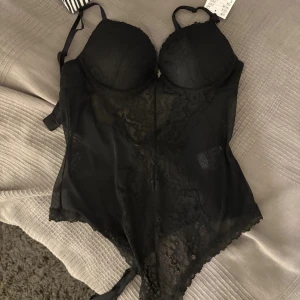 Svart spetskorsett med PUSH UP - Säljer en svart korsett från H&M med tunna axelband, bygelkupor och vacker spetsdetalj framtill. Modellen är figurnära och har transparenta partier i mesh och spets, vilket ger en snygg och trendig look. Perfekt att styla under kavaj eller med jeans. Helt oanvänd!