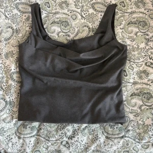 Mörkgrå korsettopp från Zara - Säljer en mörkgrå korsettopp från Zara med breda axelband och snygg drapering framtill. Toppen har en croppad passform och är tillverkad i ett slätt tyg som ger en stilren look. Perfekt att styla med jeans eller kjol för en trendig outfit.