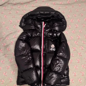 Moncler Montbeliard -                     !!!GRATTIS  FRAKT via Snabbaffär!!!        Tjena! Nu säljer jag en svart Moncler Montbeliard pufferjacka i storlek 2 (M). Passar perfekt om du är mellan 177–182 cm. Jackan har en jätte liten fläck (se bild 3), men om luvan hänger ner på jackan så syns den inte. Perfekt för kalla dagar – både varm och riktigt snygg i streetstil. Känn dig fri att ställa frågor eller lägga ett bud direkt!❤️