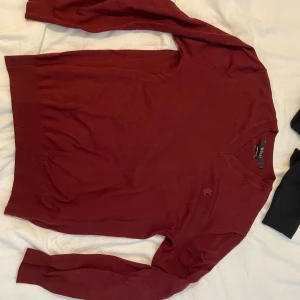 Vinröd stickad tröja Tiger of Sweden - Snygg vinröd stickad tröja från Tiger of Sweden i storlek M. Tröjan har v-ringad hals och lång ärm, med diskret broderad logga på bröstet. Tillverkad av fin italiensk ull, perfekt för dig som gillar stilrena och klassiska plagg.