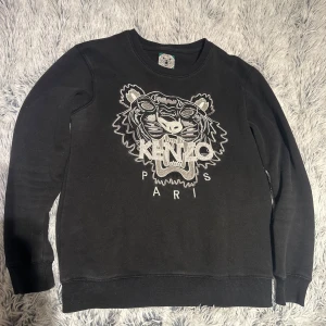 Kenzo sweatshirt - Svart sweatshirt från Kenzo med tigerhuvud och logga på bröstet. Tröjan har rund hals, långa ärmar och ribbade muddar. (Litet hål på armen, visas på sista bilden)