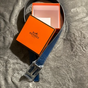 H Bälte Mörkblå - Snyggt blått skärp från H med klassiskt stort H-spänne i silverfärgad metall. Bältet är gjort i exklusivt skinn med vit kontrastsöm och har en svart baksida. Perfekt accessoar för att lyfta din outfit. Låda Följer med Samt verktyg för att justera hål. 110 Cm