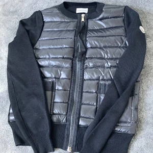 Svart Moncler cardigan jacka - Svart cardigan jacka från Moncler som är glansig. Jag köpte den på plick men skicket är som nytt. Lånade bilder, fråga om egna🩷🩷 storlek 2 men den sitter som en XS/S (Fråga även om bild på orderbekräftelsen om ni vill se, har även kvar prislappen m.m och det kommer skickas med) 