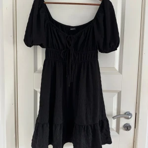 Svart kort klänning från Gina Tricot - Supersöt svart kort klänning från Gina Tricot med puffärmar, v-ringning och knytning framtill. Oanvänd 🖤