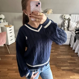 Marinblå kabelstickad tröja från SHEIN - Säljer en marinblå kabelstickad tröja dock från SHEIN så säljer billigt, med vit broderad logga på bröstet. Tröjan har v-ringad hals med vita ränder🤍