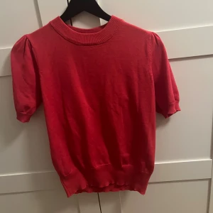 Röd kortärmad tröja Saint Tropez - Snygg röd tröja från Saint Tropez med kort puffärm och ribbad halsringning. Modellen är rak med bred mudd nertill och vid ärmslut. Perfekt till både jeans och kjol för en trendig look.