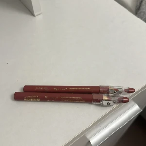 Brunrosa läppenna 2 st - Två stycken läppennor i en snygg brunrosa nyans. Pennorna har guldtext och genomskinligt lock med inbyggd pennvässare. Perfekt för att definiera läpparna och skapa en fylligare look. Säljer 2 för 49 1 för 29.