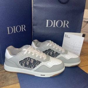 Dior B27 Uptown Low-Top Sneaker - Skorna är i mycket gott skick då dom är oanvända, förpackning har bara öppnats. Box, påse och dustbag ingår. Dessutom kommer de med ett extra par vita skosnören.                    Storlek 44                                                                 Pris kan diskuteras vid smidig affär.               Kontakta gärna vid funderingar eller vid önskemål.