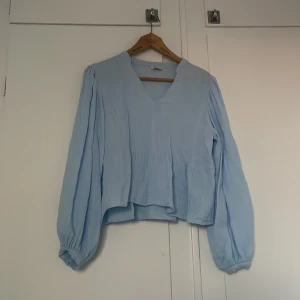 Ljusblå blus från Cubus med v-ringning - Säljer en ljusblå blus från Cubus i storlek M. Blusen har v-ringad hals, långa puffiga ärmar med resår vid ärmslut och en lös passform. Materialet känns lätt och luftigt, perfekt för vår och sommar. Enkel och stilren design som är lätt att matcha.