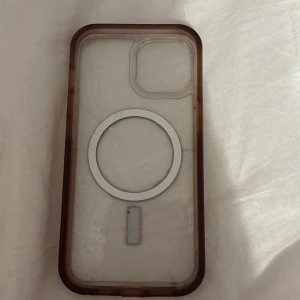 MagSafe Skal till iPhone 15 - Transparent MagSafe-kompatibelt skal för iPhone 15. Skalet har bruna kanter och viss missfärgning samt tecken på slitage, men är helt och skyddar telefonen effektivt. Perfekt för dig som vill ha trådlös laddning och extra skydd.