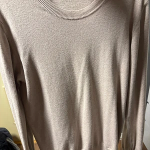 Beige kofta från Oscar Jacobson - Snygg och stilren beige tröja från Oscar Jacobson. Tröjan har rund halsringning, långa ärmar och en klassisk passform. Perfekt för dig som gillar en clean och tidlös look.