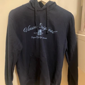 Mörkblå hoodie Vinson Original - Mörkblå hoodie från Vinson Original med vit text på bröstet. Klassisk känguruficka framtill, snörning i huvan och långa ärmar. Perfekt för en chill och avslappnad stil. Har lite glitter inte fläckar på. 