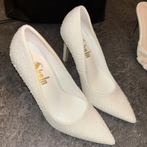 Vita pumps med pärldetaljer från Shein - Säljer ett par vita pumps från Shein med spetsig tå och hög klack. Skorna är täckta av små pärlliknande detaljer som ger en glittrig känsla. Perfekta för dig som vill sticka ut med eleganta och trendiga skor.