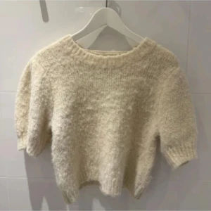 Beige fluffig stickad tröja - Supermjuk och fluffig stickad tröja i beige med kortare ärmar och rund hals. Perfekt för lager-på-lager och ger en mysig vibe till din outfit.