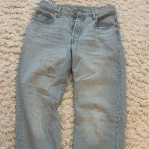 Levi's 501 ljusblå jeans 90s - Ljusblå Levi's 501 jeans från Premium-kollektionen, 90s-modell. Klassisk rak passform med fem fickor och knappgylf. Jeansen har slitna detaljer och små hål på benen för en cool vintagekänsla. Perfekta för dig som gillar retrostil. Dessa har jag bara använt en gång. Ordinarie pris: 1149kr