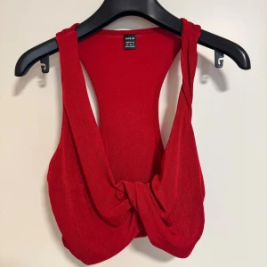 Röd twistad linnetopp från SHEIN - Säljer en snygg röd linnetopp från SHEIN med twistad detalj framtill. Toppen är ärmlös och har breda axelband, perfekt för att skapa en cool och trendig look. Materialet är mjukt och stretchigt för skön passform.