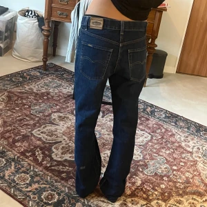 Gul&Blå mörkblå jeans i straight passform - Mörkblå Gul&Blå jeans med klassisk femficksdesign och straight-passform. Jeansen har låg midja och raka ben som blir lite vidare nertill. Tillverkade i robust denim med snygga kontrastsömmar och Levi's-patch bak i midjan.