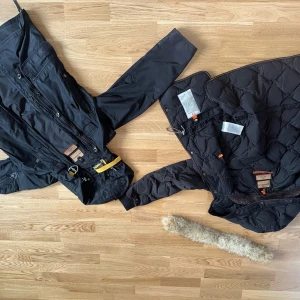 Svart Parajumpers parkajacka XS - Svart parkajacka från Parajumpers med avtagbar fuskpäls på huvan, flera fickor, dragkedja och knappar framtill samt ikonisk gul rem vid kragen. Jackan är quiltad på insidan och har lång ärm. Perfekt för kalla dagar. Pris kan diskuteras😁😁