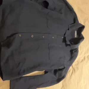 Mörkblå skjorta från Dressmann 2XL - Snygg mörkblå skjorta från Dressmann i storlek 2XL. Skjortan har klassisk krage, knäppning framtill och två bröstfickor. Perfekt för dig som gillar en stilren och enkel look. Materialet känns mjukt och bekvämt mot huden.