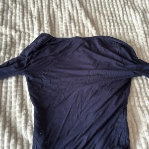 Mörkblå långärmad v-ringad topp - Snygg mörkblå topp från Gina Tricot med v-ringad hals och långa ärmar. Modellen är slim och sitter snyggt på kroppen. Perfekt att matcha med jeans eller kjol för en cool look. Materialet är mjuk bomull som känns skönt mot huden.