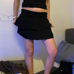 Svart volangkjol med resårmidja - Säljer en svart kortkjol med dubbla volanger och bred resår i midjan. Kjolen har en mjuk och skön känsla, perfekt för dig som gillar en enkel men snygg look. Passar dig som vill ha en kjol med lite extra volym och rörelse.