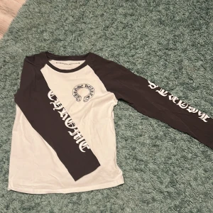 Chrome Hearts långärmad tröja M - Säljer en långärmad tröja från Chrome Hearts i storlek M. Tröjan är vit med gråa ärmar och har tryck med Chrome Hearts-logga både fram och bak samt längs ärmarna. Materialet är mjuk bomull och modellen har en klassisk rund hals.