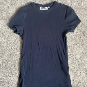 Marinblå ribbad t shirt Weekday - Säljer en enkel och snygg marinblå ribbad T-shirt från Weekday. Modellen är kort med rund hals och korta ärmar, perfekt för dig som gillar en clean och chill stil. Materialet är mjukt och stretchigt, vilket gör den skön att bära hela dagen.