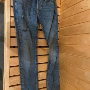 Blå jeans från Jack & Jones - Klassiska blå jeans från Jack & Jones med raka ben och snyggt sliten look. Jeansen har fem fickor, normal passform och är tillverkade i bomull. Perfekta för dig som gillar en avslappnad stil.