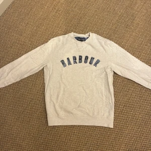 Beige sweatshirt från Barbour M - Säljer en beige sweatshirt från Barbour i storlek M passar även S. Tröjan har rund hals, långa ärmar och ett stort blått Barbour-tryck över bröstet. Tillverkad i mjuk bomull, perfekt för chill dagar. Klassisk och enkel stil med snygga detaljer vid halsen.
