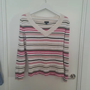 Randig ribbad tröja - Randig långärmad tröja från äldre Lindex i ribbad bomull. Färgerna är beige, vit, rosa och khakigrön. Tröjan har v-ringad hals. 🩷