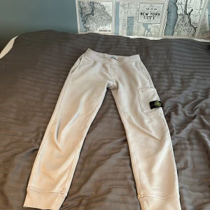 Beige mjukisbyxor från Stone Island - Snygga beige mjukisbyxor från Stone Island Junior med klassisk logga på benet. Byxorna har resår i midjan, ribbade muddar vid bensluten och en praktisk ficka på sidan. Perfekta för en chill och avslappnad stil. Perfekt för en mysig höstkväll.